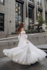 Wall Mural - Vertical portrait of young just married lady dressed in long stunning white dress. Professional wedding photo shooting. Posing city outdoors