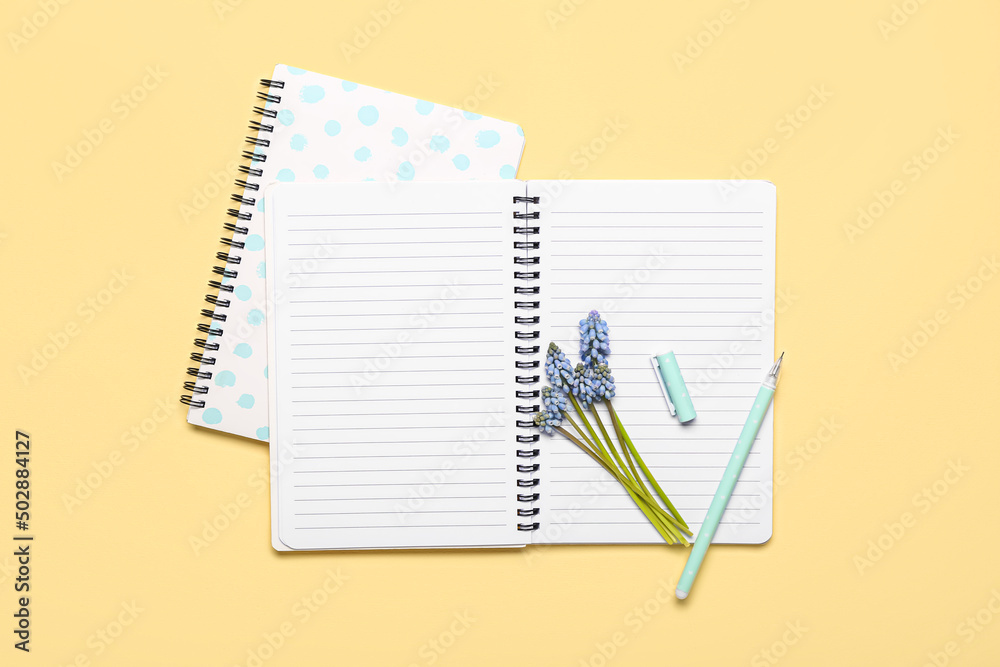 Notebooks with beautiful Muscari flowers on light yellow background