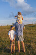 © Alina - Father with children on shoulders outdoors. Family in nature in the village concept