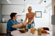 © Drazen - Happy gay woman serving food to her girlfriend while having meal together in dining room.