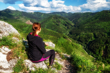 Canvas Print - Hiking girl sitting on top of the hill and looking on mountains