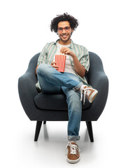 people and furniture concept - happy smiling young man in glasses with popcorn sitting in chair over white background