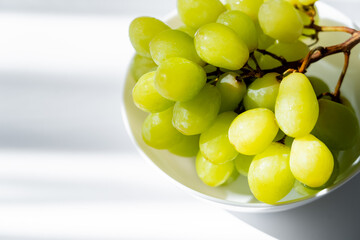 Wall Mural - sunshine on green grapes in bowl on white.