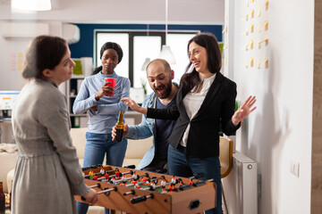 Wall Mural - Cheerful woman winning foosball table game play in office, meeting to have drinks after work. Business people playing soccer match and having fun with alcoholic beverage and snacks.