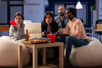 Wall Mural - Diverse group of coworkers having fun with video games on console, enjoying drinks and snacks at office celebration after work hours. People using controller to play online game at gathering.