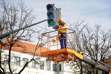 Man In Uniform On Aerial Platform Fix And Repair Broken Traffic Signal. Traffic Lights Repair Works, Worker In Lift Bucket Working At Height. Maintenance Of Public Lighting And Urban Traffic Signals