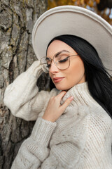 Wall Mural - Autumn portrait of a beautiful stylish woman with vintage eyewear, hat and knitted sweater in an autumn park near a tree