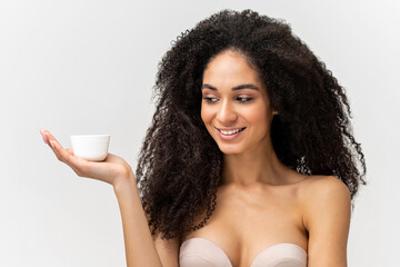 Wall Mural - Portrait view of the multiracial curly woman with perfect skin holding tube with cosmetic cream and looking on it with pleasure smile