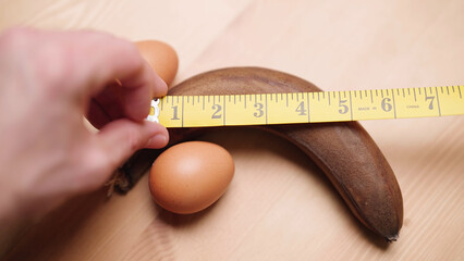 Person with measuring tape measure manhood size of black banana with eggs