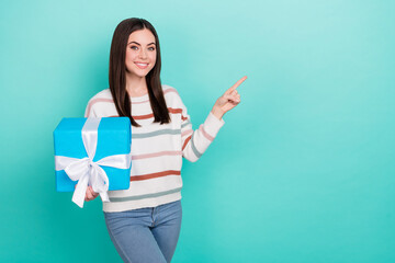 Poster - Photo of cute charming lady hold gift finger indicate empty space wear striped pullover isolated blue color background