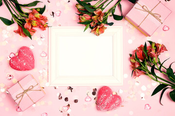 Wall Mural - Empty white photo frame with flowers, hearts, gifts and confetti  on pink background.