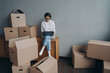 © VK Studio - Spanish business lady rents apartment. Happy girl is sitting among boxes and working on laptop.