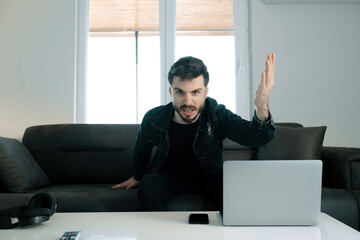 Wall Mural - Frustrated young man, man sitting on sofa in living room and getting angry at camera, he is very angry with the result of the match and shows it with his hand gesture