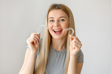 Wall Mural - Happy girl with white smile holding transparent removable retainer. Bite correction device.