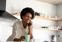 Smiling Mid Adult African American Woman Talking On Smart Phone While Having Coffee In Kitchen