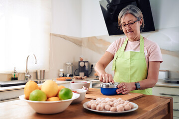 Adult woman, cooking a Spanish dish, estofado de albóndigas. Cutting the onion at that moment. Wearing an apron, carrying glasses and cooking utensils.