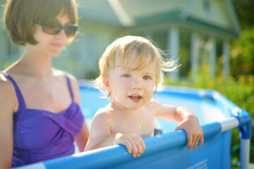 Cute teenage sister and her toddler brother having fun in outdoor pool. Child learning to swim. Kid having fun with water toys. Family fun in a pool.