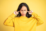 Fototapeta Tęcza - asian woman with annoyed expression covering ears with both hands on isolated background