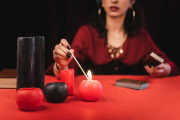 Wall Mural - Cropped view of blurred medium burning candle and holding tarot cards isolated on black.