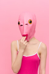Wall Mural - Funny woman in a sexy costume with a pink fish mask on her head put her fingers in her mouth in pink clothes on a pink background. The concept of modern art photography