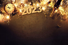 New Years Eve 2023 Holiday Background With Fir Branches, Clock, Christmas Balls, Champagne Bottle, Gift Box And Lights