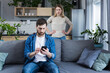 © Liubomir - Conflict, young couple, family, man and woman. An angry woman shouts at a man who constantly uses and plays on the phone, does not pay attention