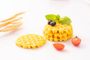 Wall Mural - Waffle pieces garnished with blackberries and mint, and a slices cherry tomato on a white background