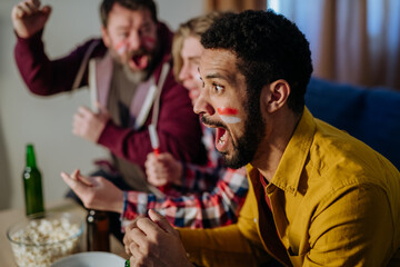 Wall Mural - Close-up of excited football fan watching match with friends at home.