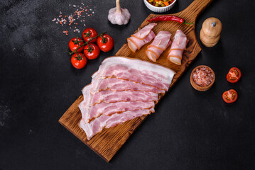 Slices of delicious raw or salted bacon with spices, salt, vegetables and herbs on a wooden cutting board