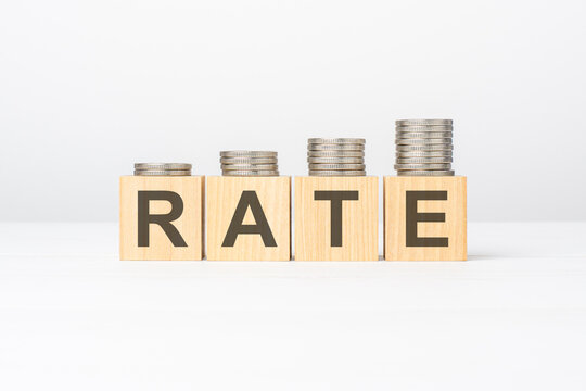 Rate text written on wooden block with stacked coins on white background