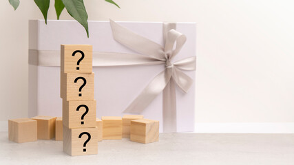 Sticker - four cubes with question marks on the white surface of a gift box tied with a light festive ribbon