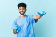 © luismolinero - Moroccan dentist man holding tools isolated on blue background giving a thumbs up gesture