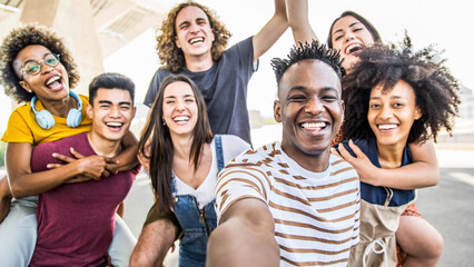 Wall Mural - Group multiracial friends taking selfie picture with mobile smartphone outside - Happy young with hands up laughing at camera - Youth concept with guys and girls having fun walking on city street