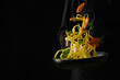 A professional chef in a black uniform prepares Italian pasta with seafood and vegetables on a black background. Close-up, bright colors. There is free space to insert. Banner.