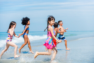 Group of Diversity little child boy and girl friends running and playing in sea water on tropical beach together on summer vacation. Happy children kid enjoy and fun outdoor lifestyle on beach holiday