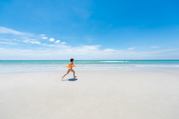 Portrait of Asian child girl in swimwear and swim ring running playing on tropical beach in sunny day. Happy little girl enjoy and fun outdoor activity lifestyle on summer travel vacation at the sea