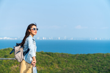 Wall Mural - Young beautiful Asian woman with backpack solo travel on tropical island mountain peak in summer sunny day. Cheerful female relax and enjoy outdoor lifestyle in summer beach holiday vacation trip