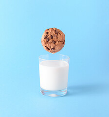 the chocolate chip cookie biscuit levitates in the air over a glass of milk on a blue background. sw