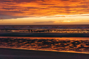 Wall Mural - Beautiful sunset with dramatic moody cloudy sky above the ocean of North Sea and silhouette of people and dogs, De Haan, Belgium.