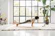 © Daniel - Young mixed race woman exercising at home doing plank pose using online video training with laptop. Copy space.
