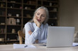 © fizkes - Serious senior business woman working at laptop computer at home, looking away, touching chin, thinking over project. Thoughtful mature homeowner woman pondering on paper document at table