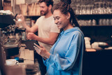 Fototapeta  - Smiled stylish young woman barista smiling and using tablet device. Learning coffee making. Gadget.