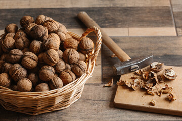 Basket full of walnuts in shell and hammer on a wooden background. Natural, healthy product. Place for text.