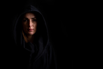 Wall Mural - Sad young woman in a black hood on a dark black background