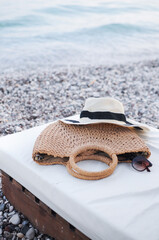 Beach flat lay accessories: straw hat, summer bag, and sunglasses on sunbed