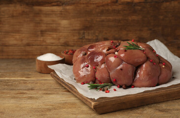 Fresh raw kidney meat with spices and rosemary on wooden table, space for text