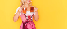 Woman In Festive German Dress Holding Two Mugs With Beer In Front Of Yellow Background.