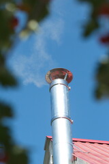 Modern chimney on the roof of house. Clean metal chimney pipe on the blue sky background.