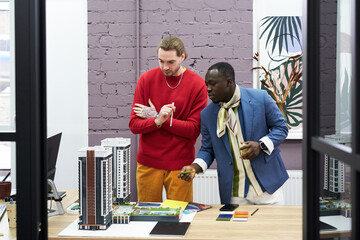 Poster - African designer in fashion jacket discussing the project of mock-up buildings together with his colleague at office