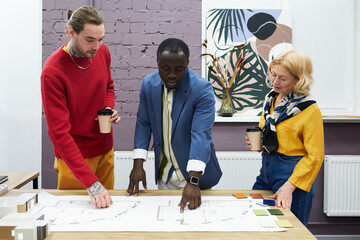 Poster - African man pointing at blueprint on table and discussing new project together with his colleagues